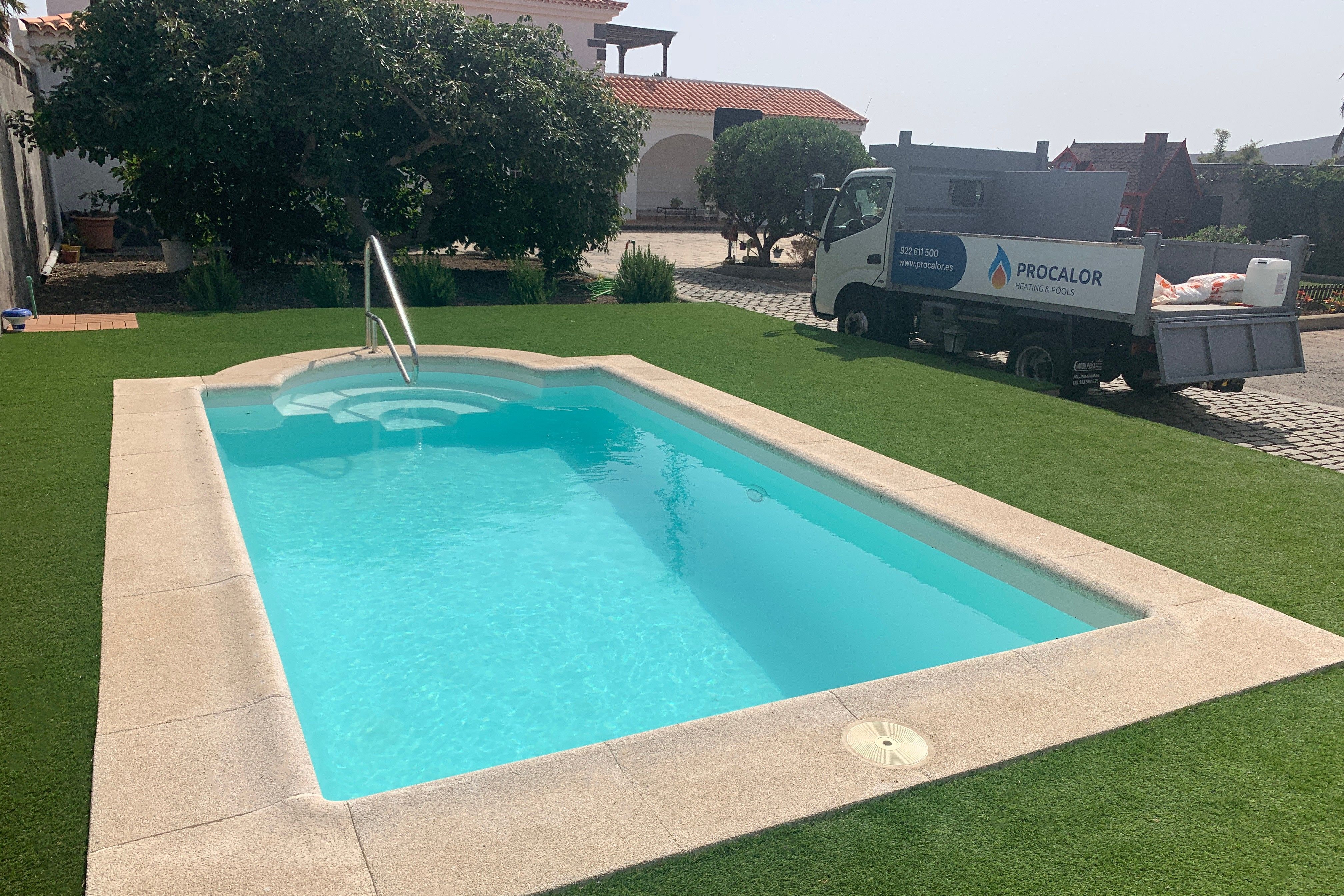 Newly installed compact pool with handrail and stone coping in a lawn garden, with the PROCALOR truck in the background